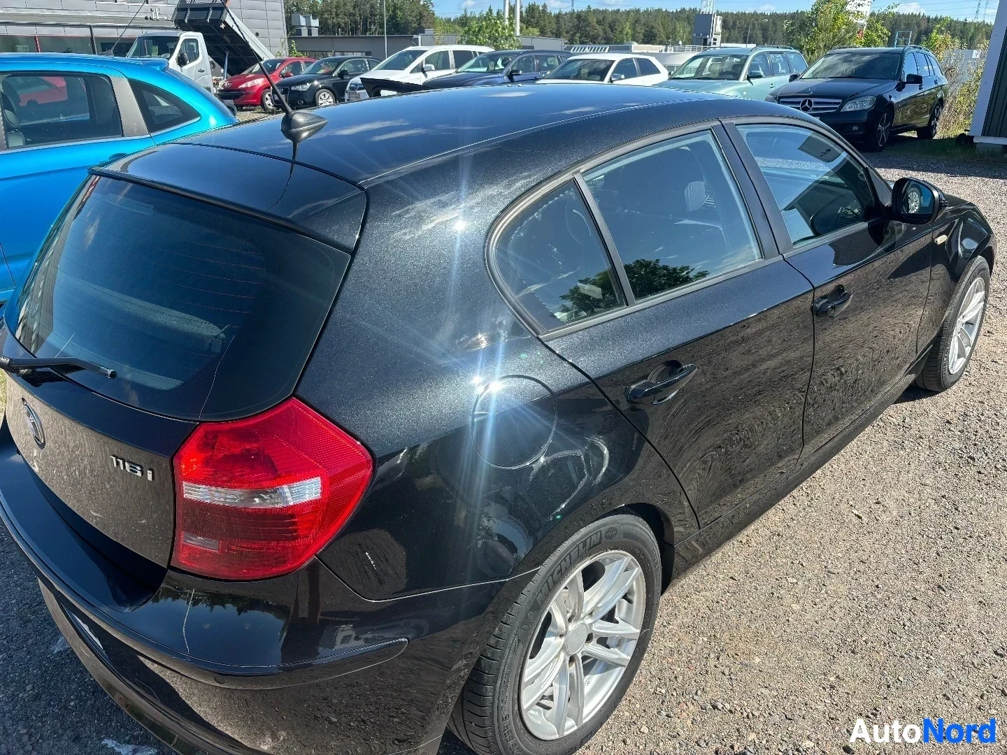 Sivulta: Musta BMW 116i Business -malli näkyy sivulta, konepelti on auki ja ovi auki. Valkoisen väriset vanteet näkyvät. Punainen takavalo on näkyvillä. Pohjan alla on h