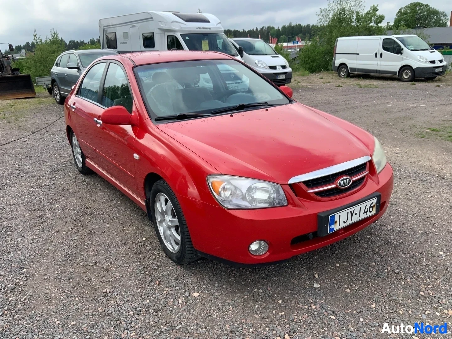 Etuviisto, nokka oikealle: Punainen Kia Cerato nelioven sedan edestä ja vasemmalta sivulta katsottuna, rekisterilevy näkyvissä
