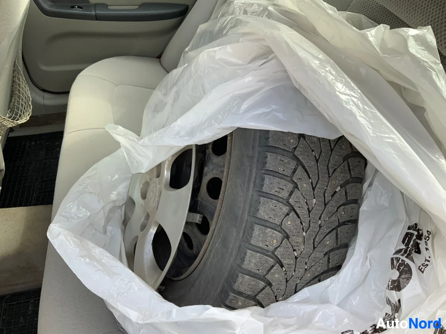 Yksityiskohta: Valkoisen koristemuovin peittämä valurenkaan ja talvirengas sisäkabiiissa, renkaan kuvio ja tummahko vantin muoto näkyvissä
