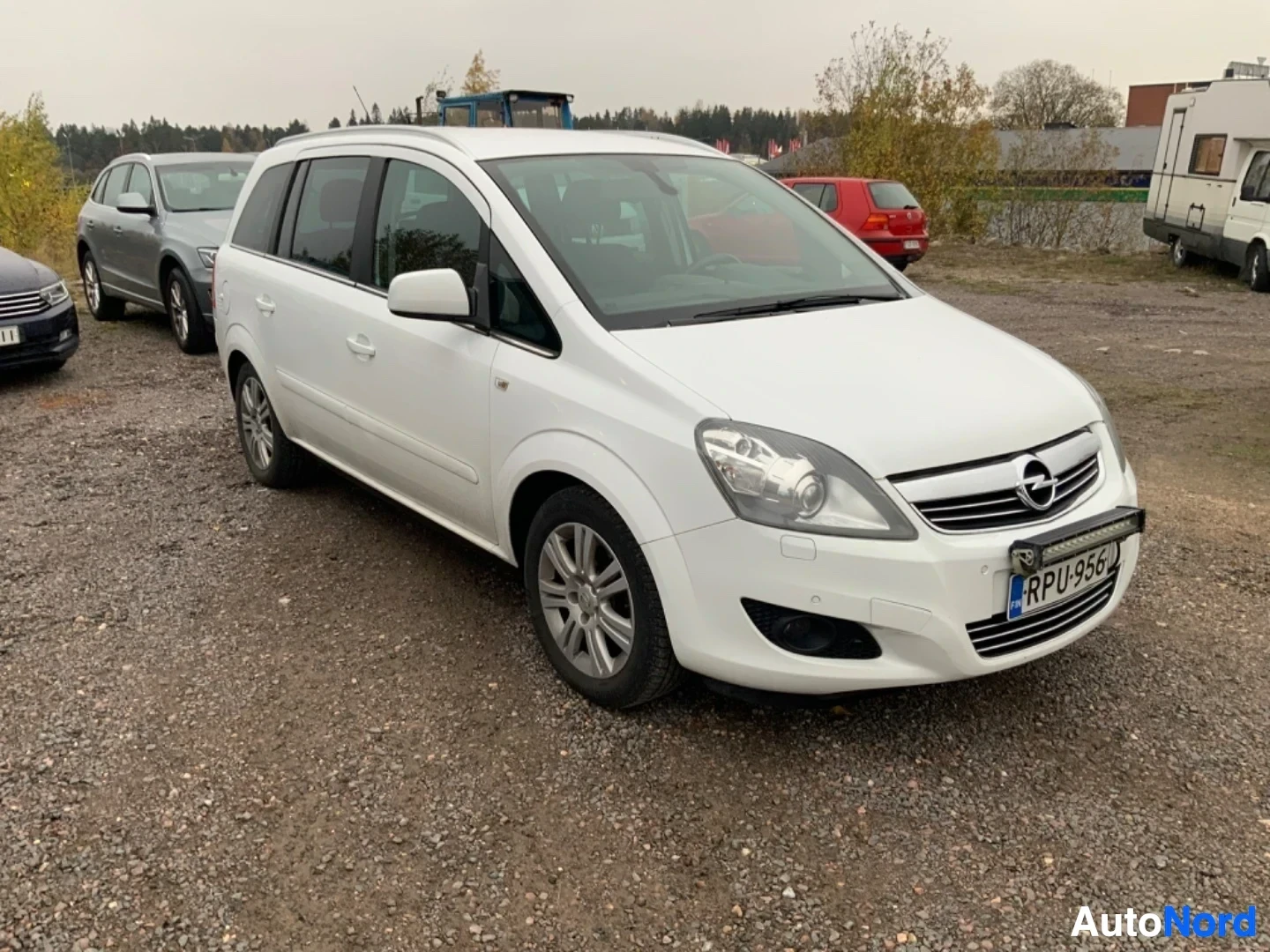 Etuviisto, nokka vasemmalle: Valkoinen Opel Zafira -tila-auto kuvattuna kolmen neljänneksen kulmasta vasemmalta, näkyvissä etusarja ja vasen sivu. Rekisterilevy näkyvissä