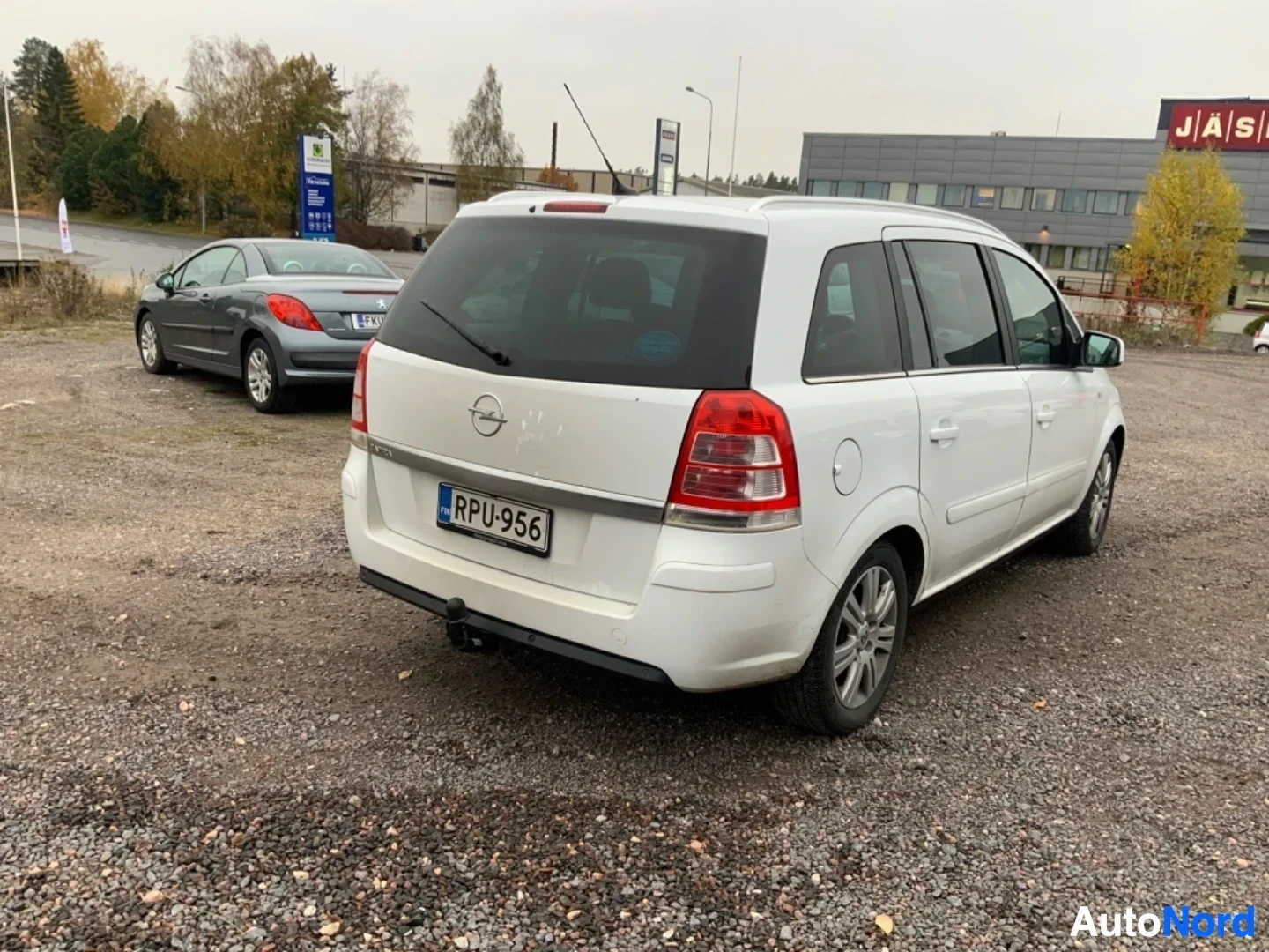 Takaviisto: Valkoinen Opel Zafira -tila-auto takakolmen neljänneksen kulmasta, näkyvissä takaosa ja oikea sivu. Rekisterilevy ja punaiset takavalot näkyvissä