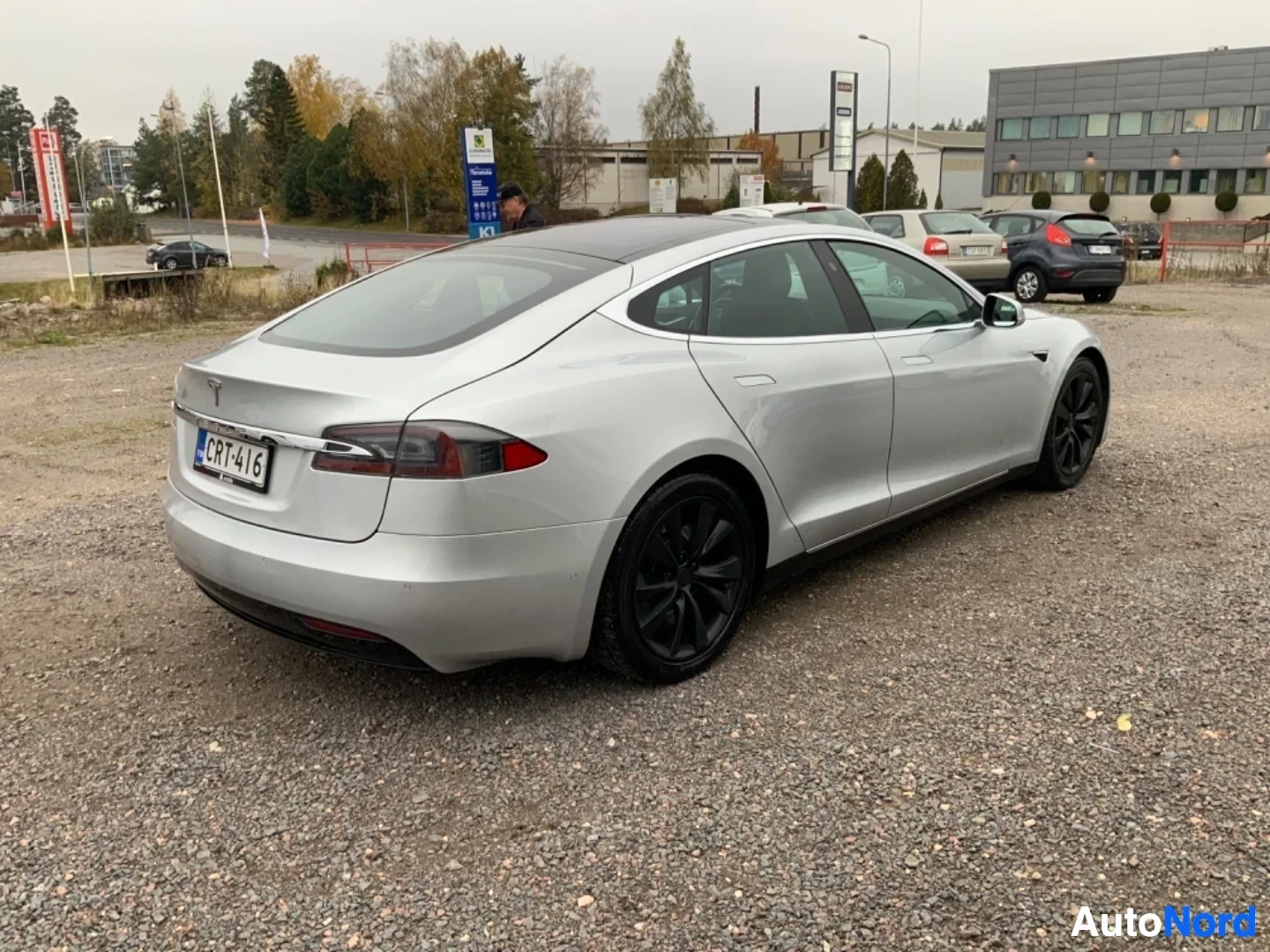 Takaviisto: Valkoinen sähköauto sivusta taaksepäin kuvattuna parkkipaikalla, rekisterikilvessä teksti