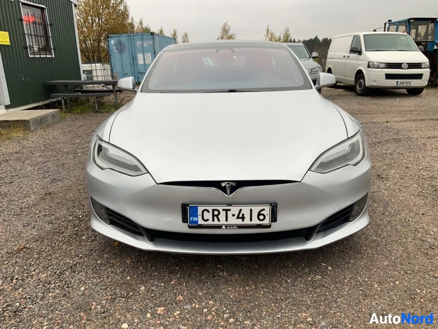 Edestä: Valkoisen Tesla-mallin etunäkymä pysäköintialueella. Rekisterilautakuva näkyy keskellä. LED-ajovalot ja mustat pyörät