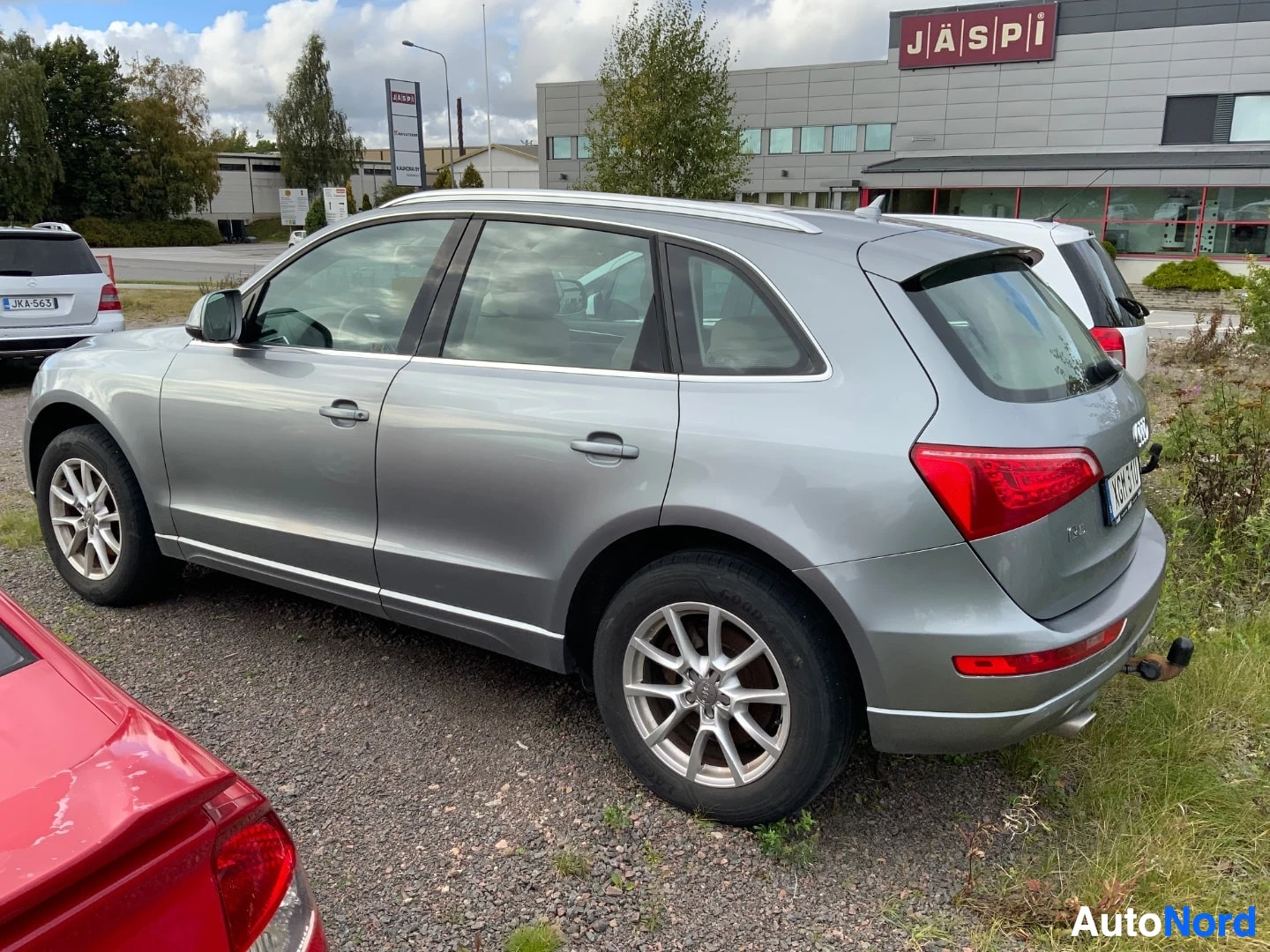Takaviisto: Harmaa Audi Q5 maastoauto pysäköitynä ulkona, auton takaosa ja vasen kylki näkyvissä. Takapuskurissa on vetokoukku.