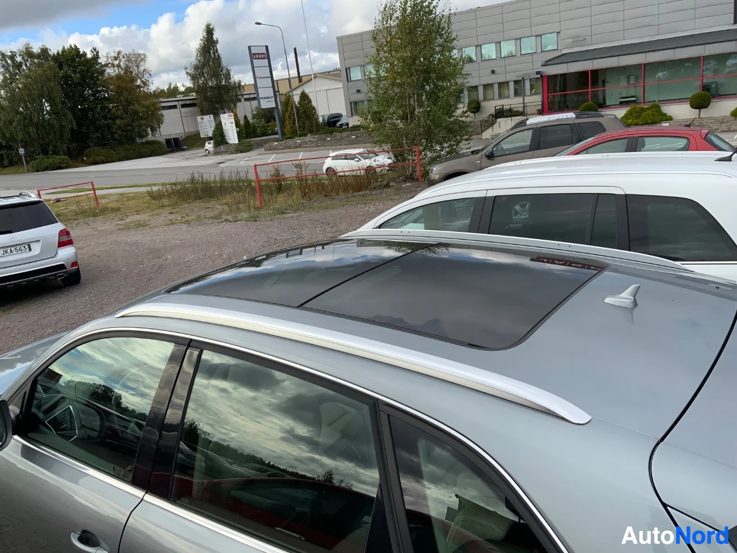 Yksityiskohta: Kuvakulma ylhäältä näyttää harmaan Audi Q5 maastoauton katon, jossa on kattokaiteet ja panoraamalasikatto.