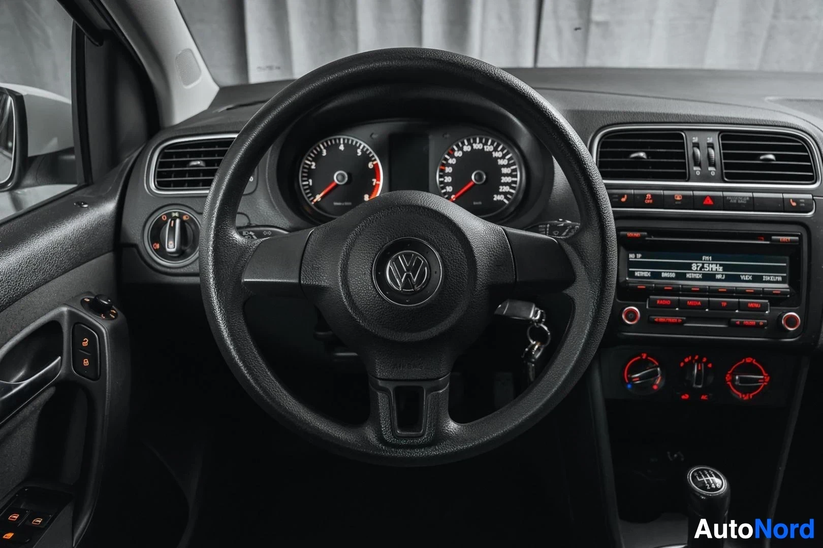 Ohjaamo: Valkoinen Volkswagen Polo, ohjauspyörä, mittaristo ja keskikonsoli kuljettajan puolelta