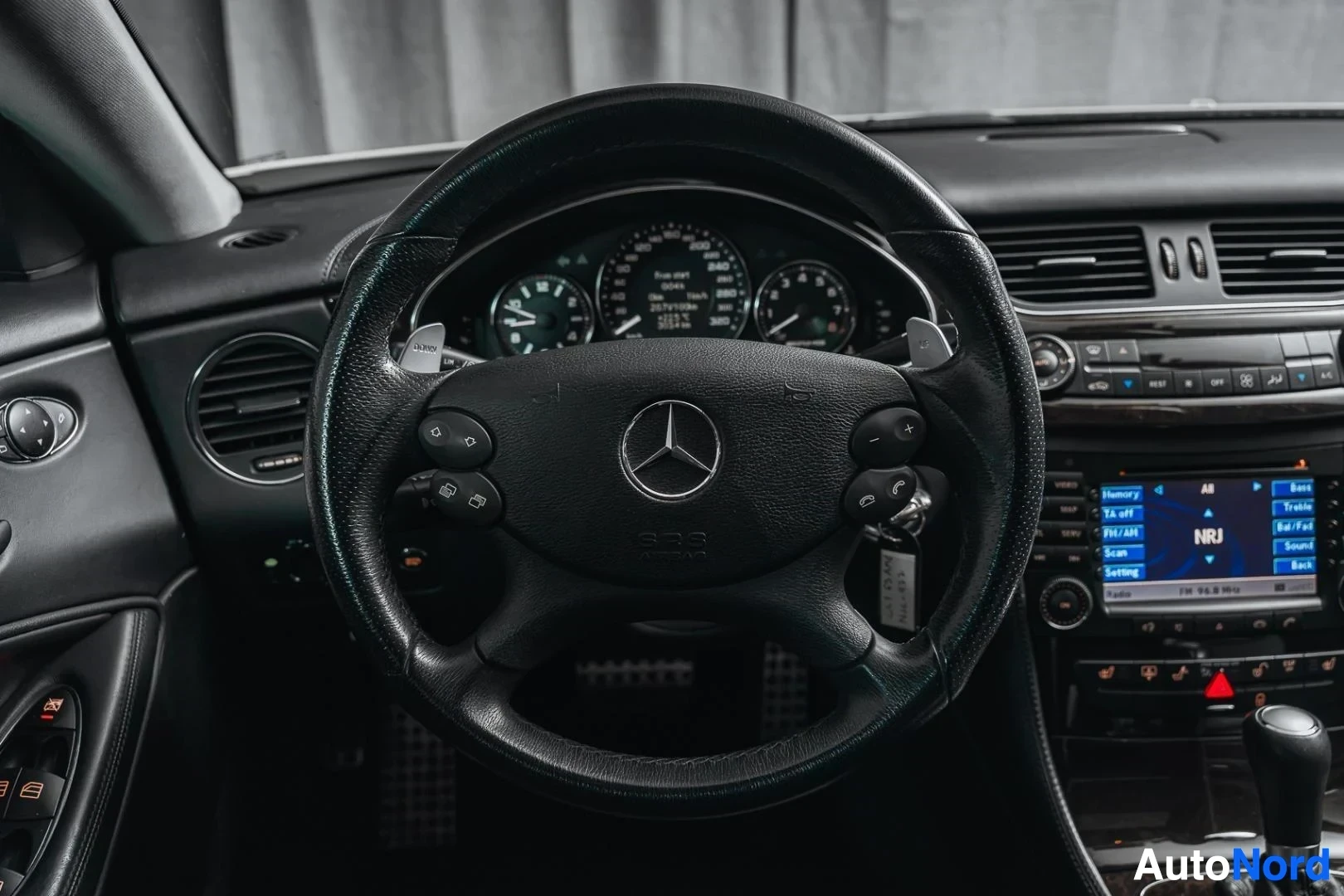 Ohjaamo: Valkoinen Mercedes-Benz CLS 63 AMG, ohjauspyörä ja mittaristo, keskinäyttö taustalla