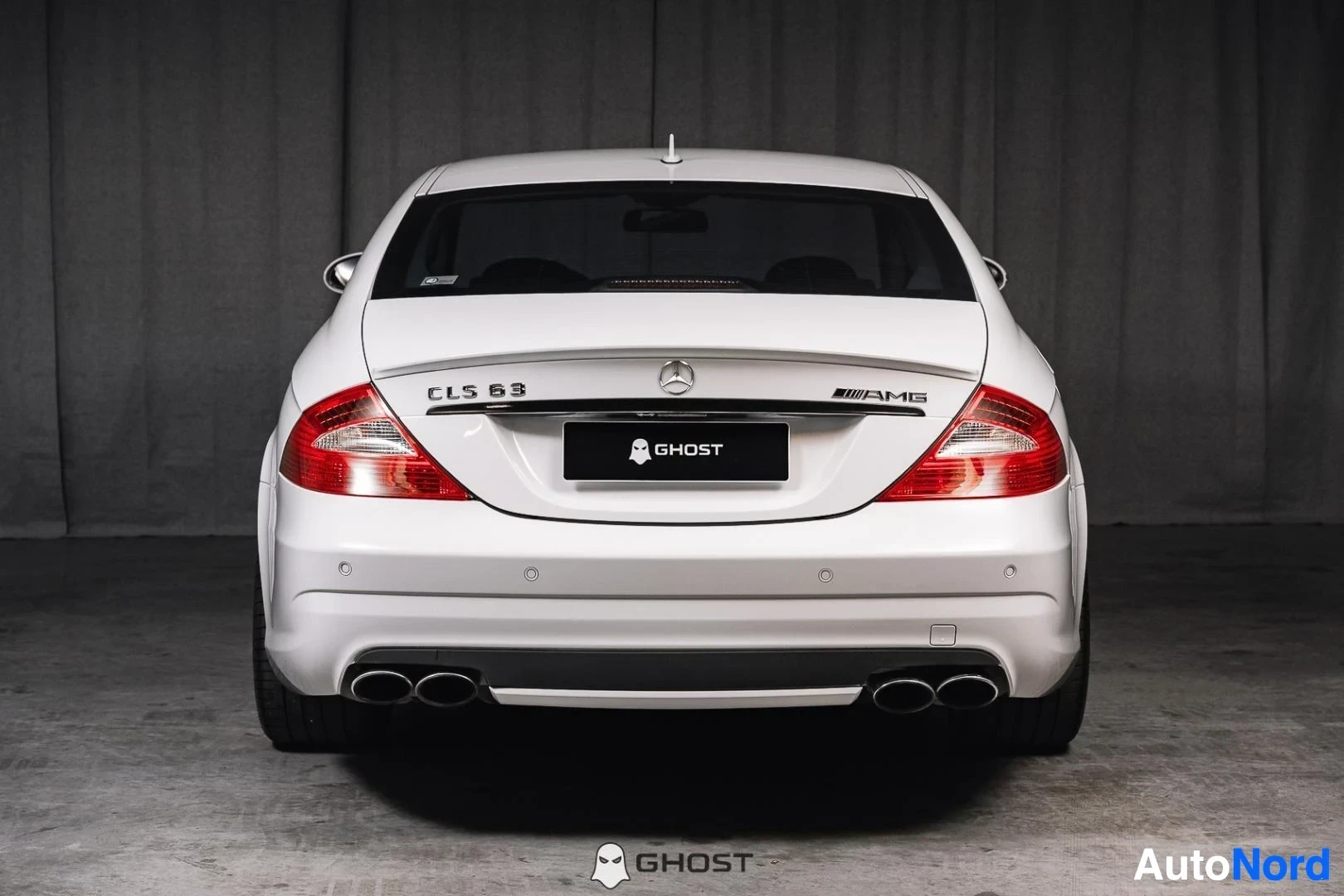 Takaa: Valkoinen Mercedes-Benz CLS 63 AMG, koko ajoneuvo näkyvissä, takavalot ja kaksoispakoputket, studiotausta