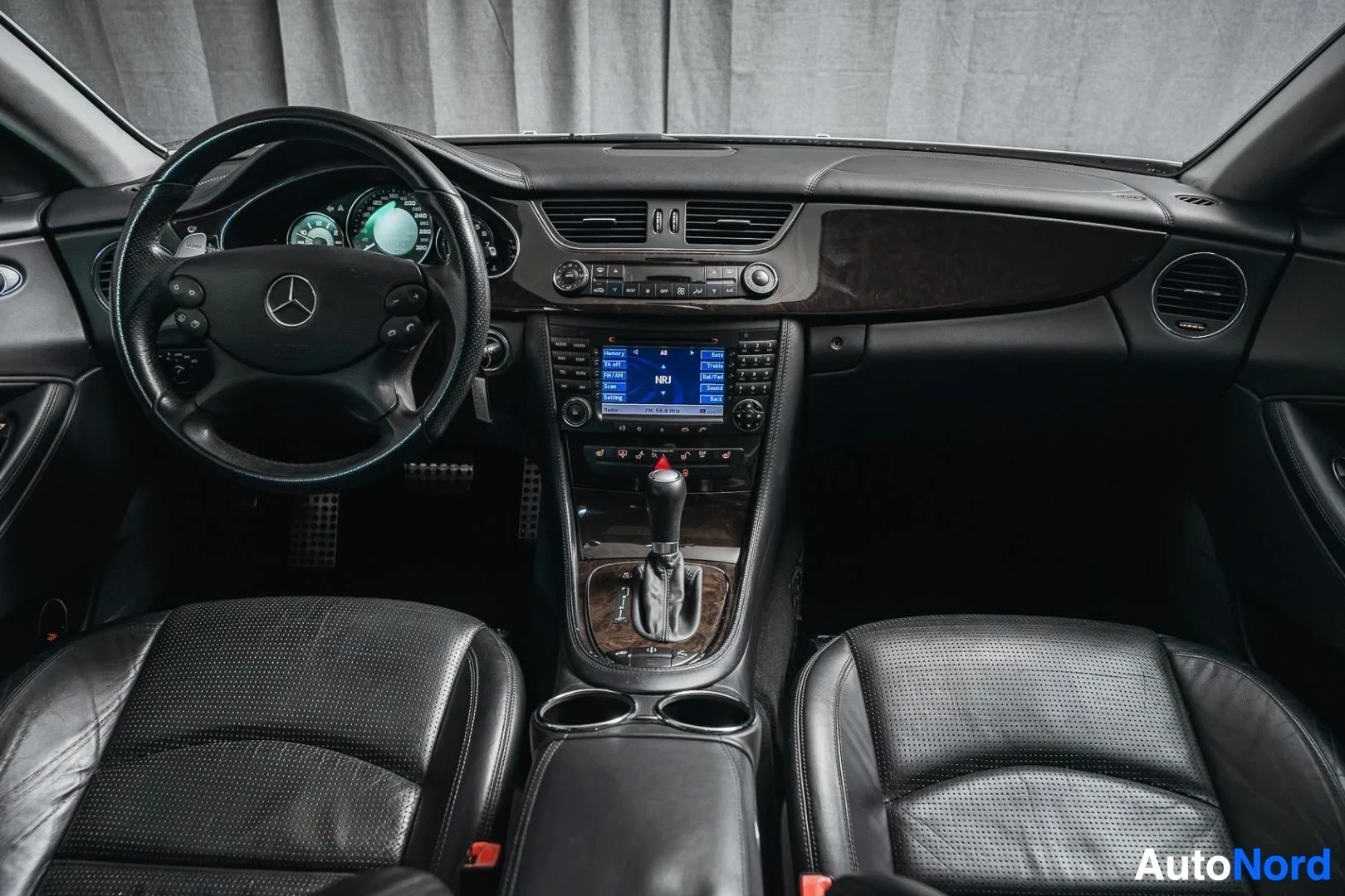 Ohjaamo: Valkoinen Mercedes-Benz CLS 63 AMG, kojelauta, ohjauspyörä, keskinäyttö, puukoristeet ja mustat nahkaistuimet