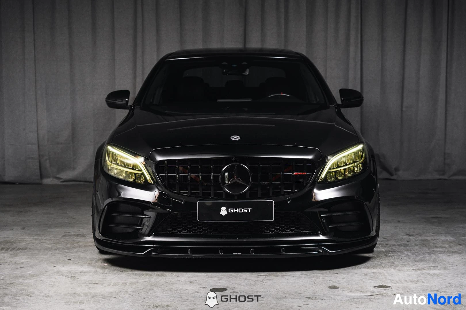 Edestä: Musta Mercedes-Benz C 43 AMG, koko ajoneuvo näkyvissä, keltaiset ajovalot, studiotausta