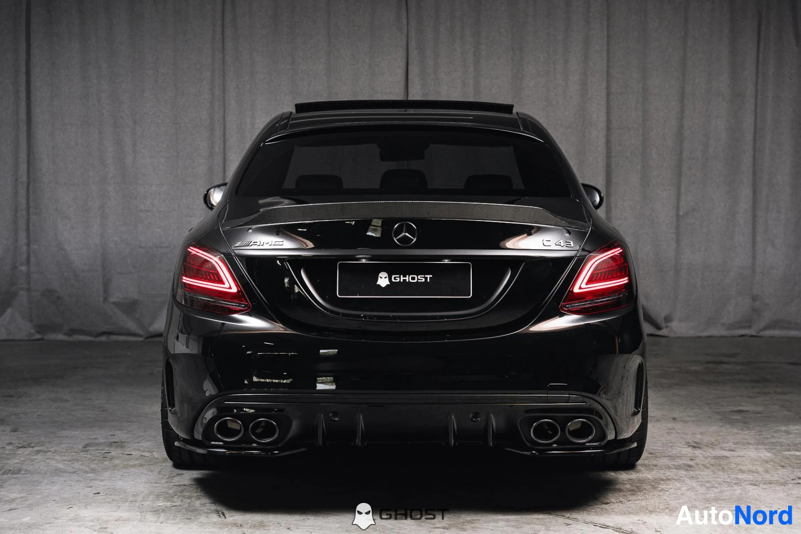 Takaa: Musta Mercedes-Benz C 43 AMG, koko ajoneuvo näkyvissä, takavalot ja kaksoispakoputket, studiotausta