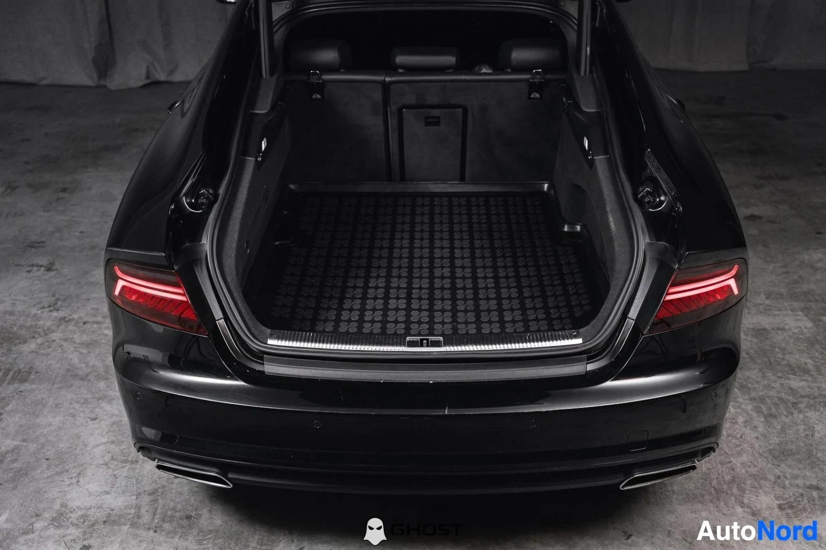 Tavaratila: Musta Audi A7, avattu takaluukku ja tavaratila kumimatolla