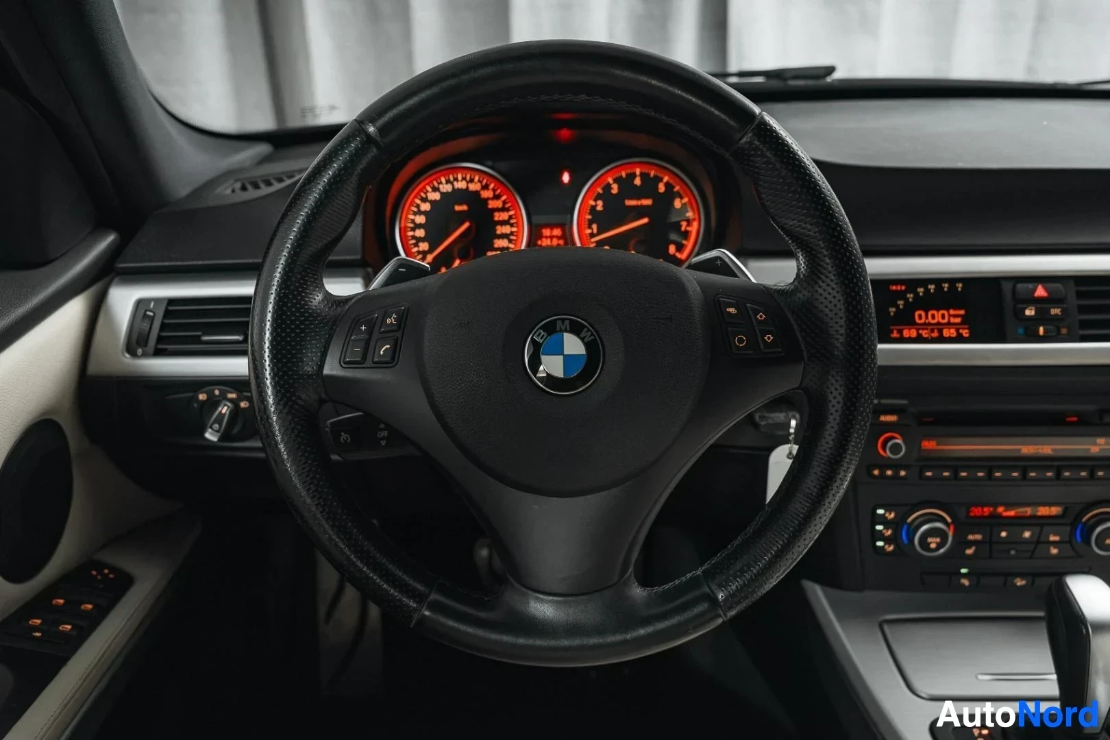 Ohjaamo: Musta BMW 335i xDrive E91 Touring, ohjauspyörä ja punaisena hehkuva mittaristo, keskinäyttö