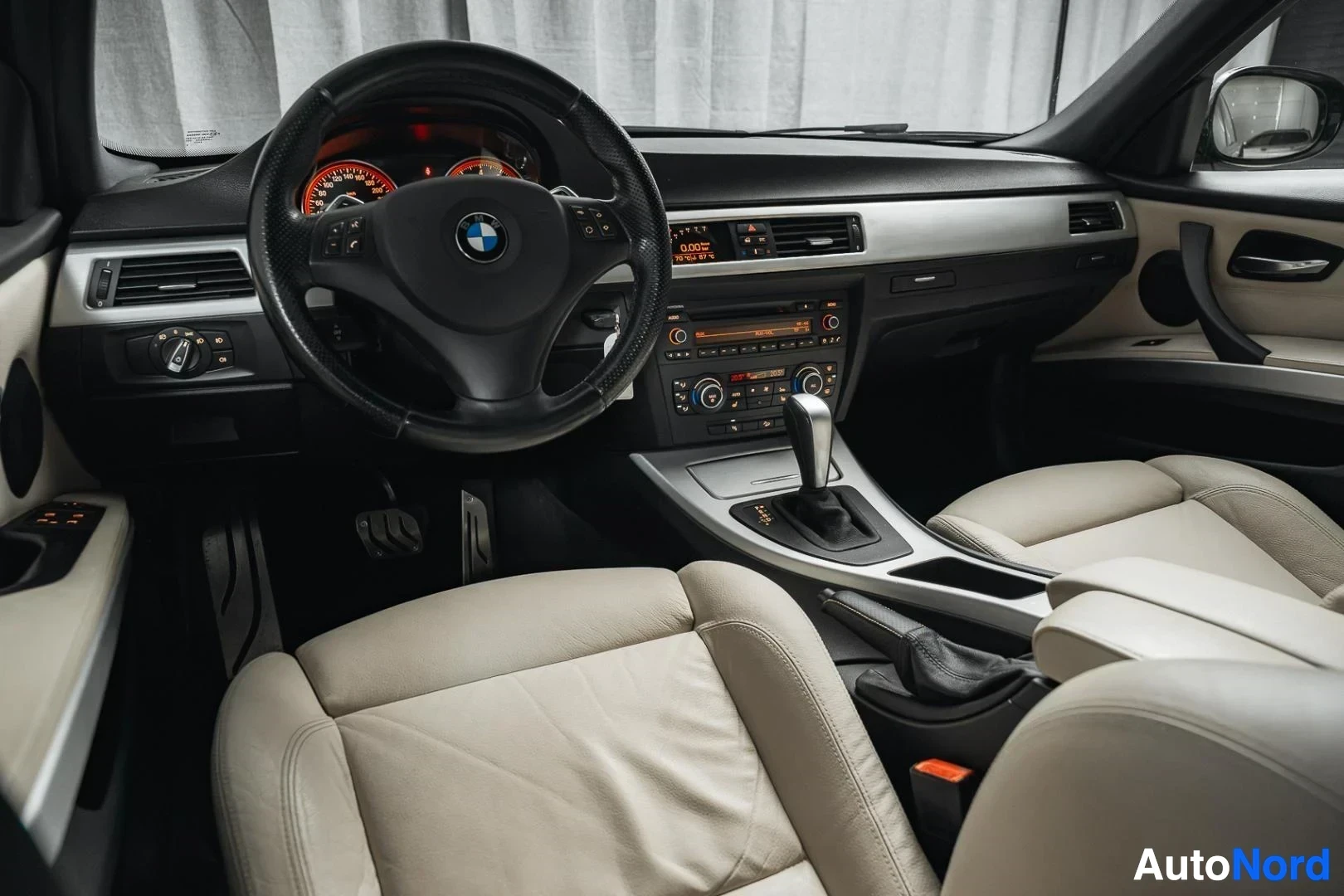 Ohjaamo: Musta BMW 335i xDrive E91 Touring, kojelauta ja etuistuimet kuljettajan ovelta kuvattuna, beige nahkaverhoilu