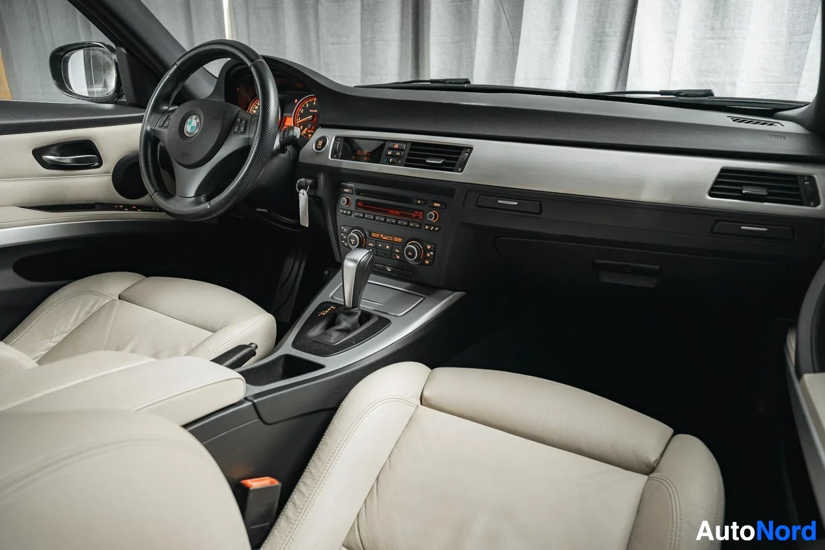 Ohjaamo: Musta BMW 335i xDrive E91 Touring, kojelauta ja etuistuimet matkustajan puolelta kuvattuna, beige nahkaverhoilu