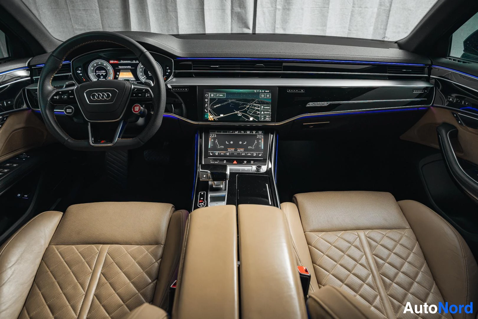 Ohjaamo: Musta Audi A8, ohjauspyörä, keskikonsoli ja beiget tikatut nahkaistuimet takaa kuvattuna