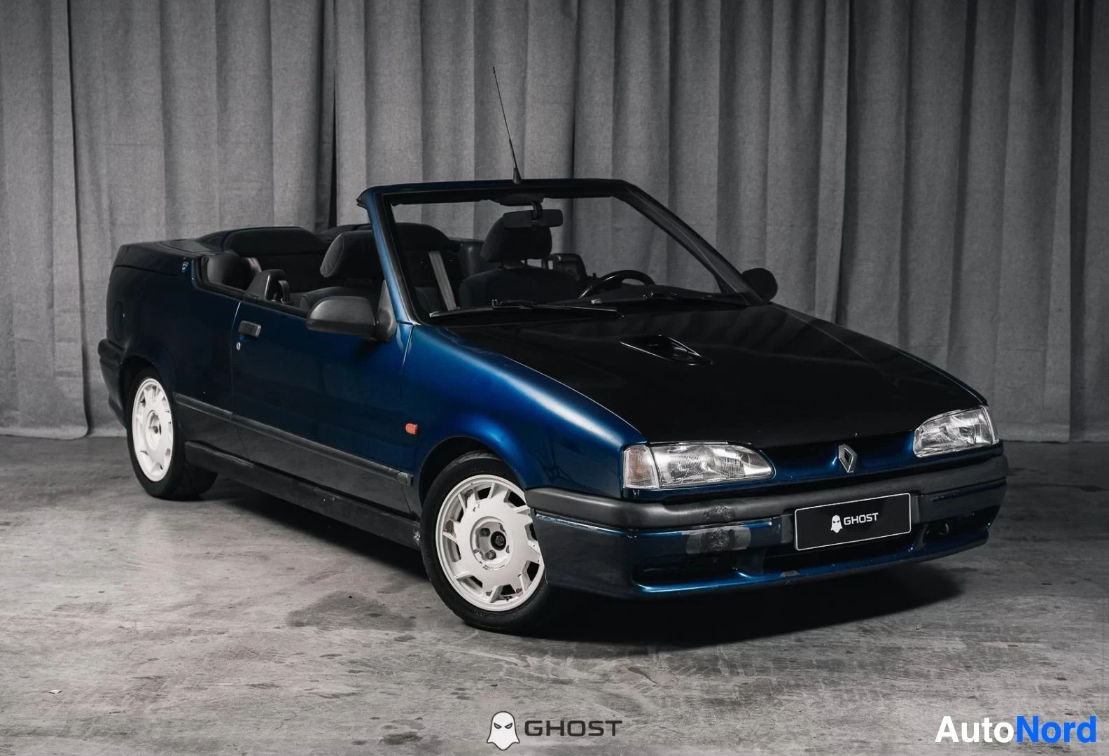 Etuviisto, nokka oikealle: Tummansininen Renault 19 Cabriolet, koko ajoneuvo näkyvissä, katto avattuna, studiotausta