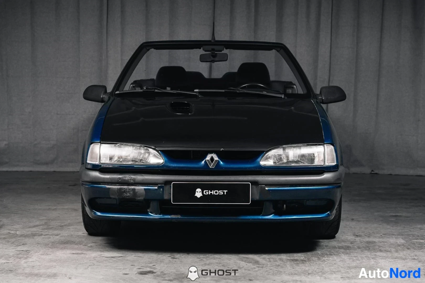 Edestä: Tummansininen Renault 19 Cabriolet, koko ajoneuvo näkyvissä, katto avattuna, studiotausta