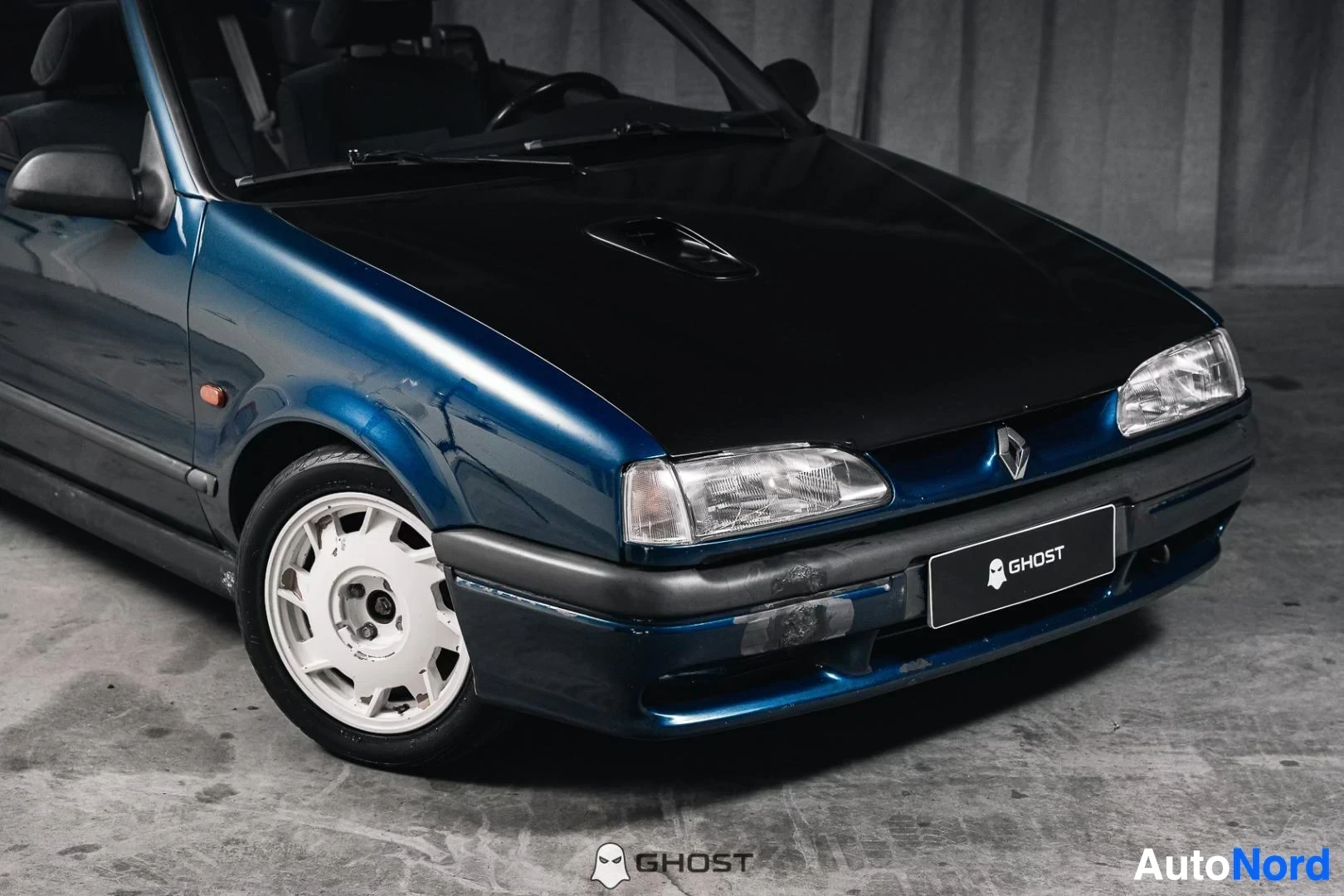 Etuviisto, nokka oikealle: Tummansininen Renault 19 Cabriolet, lähikuva keulasta ja etuvanteesta, valkoiset vanteet