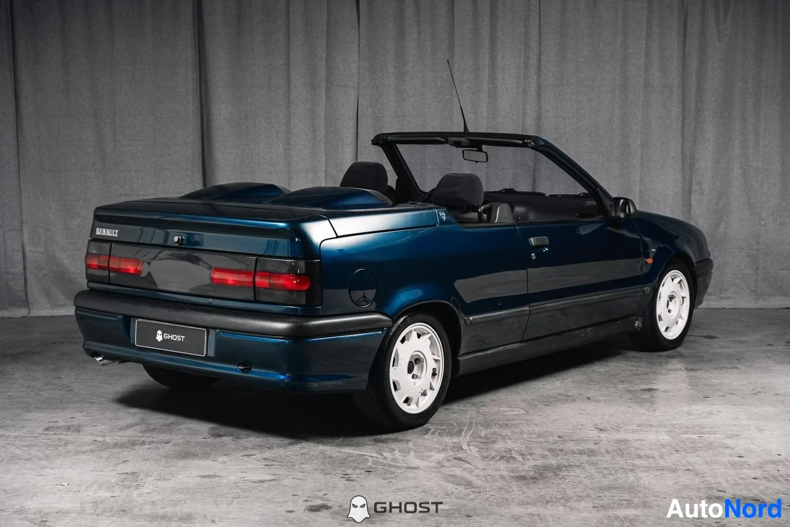 Takaviisto: Tummansininen Renault 19 Cabriolet, koko ajoneuvo näkyvissä, katto avattuna, valkoiset vanteet, studiotausta