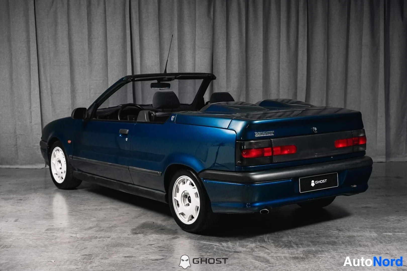 Takaviisto: Tummansininen Renault 19 Cabriolet, koko ajoneuvo näkyvissä, katto avattuna, studiotausta