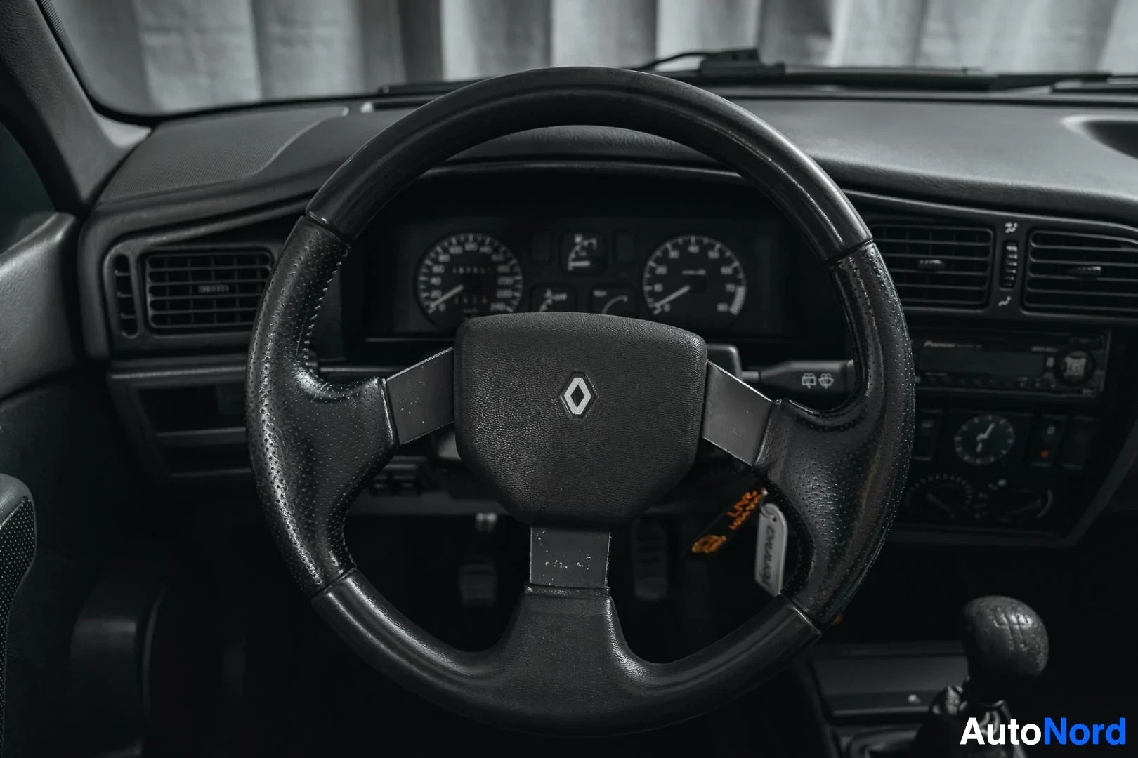 Ohjaamo: Tummansininen Renault 19, ohjauspyörä ja mittaristo kuljettajan puolelta