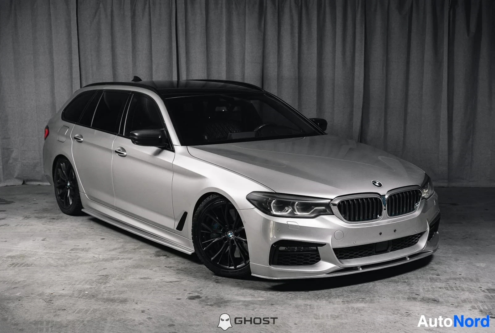 Etuviisto, nokka oikealle: Hopeanharmaa BMW 540i G31 xDrive Touring, koko ajoneuvo näkyvissä, M-Sport-paketti, mustat vanteet, studiotausta