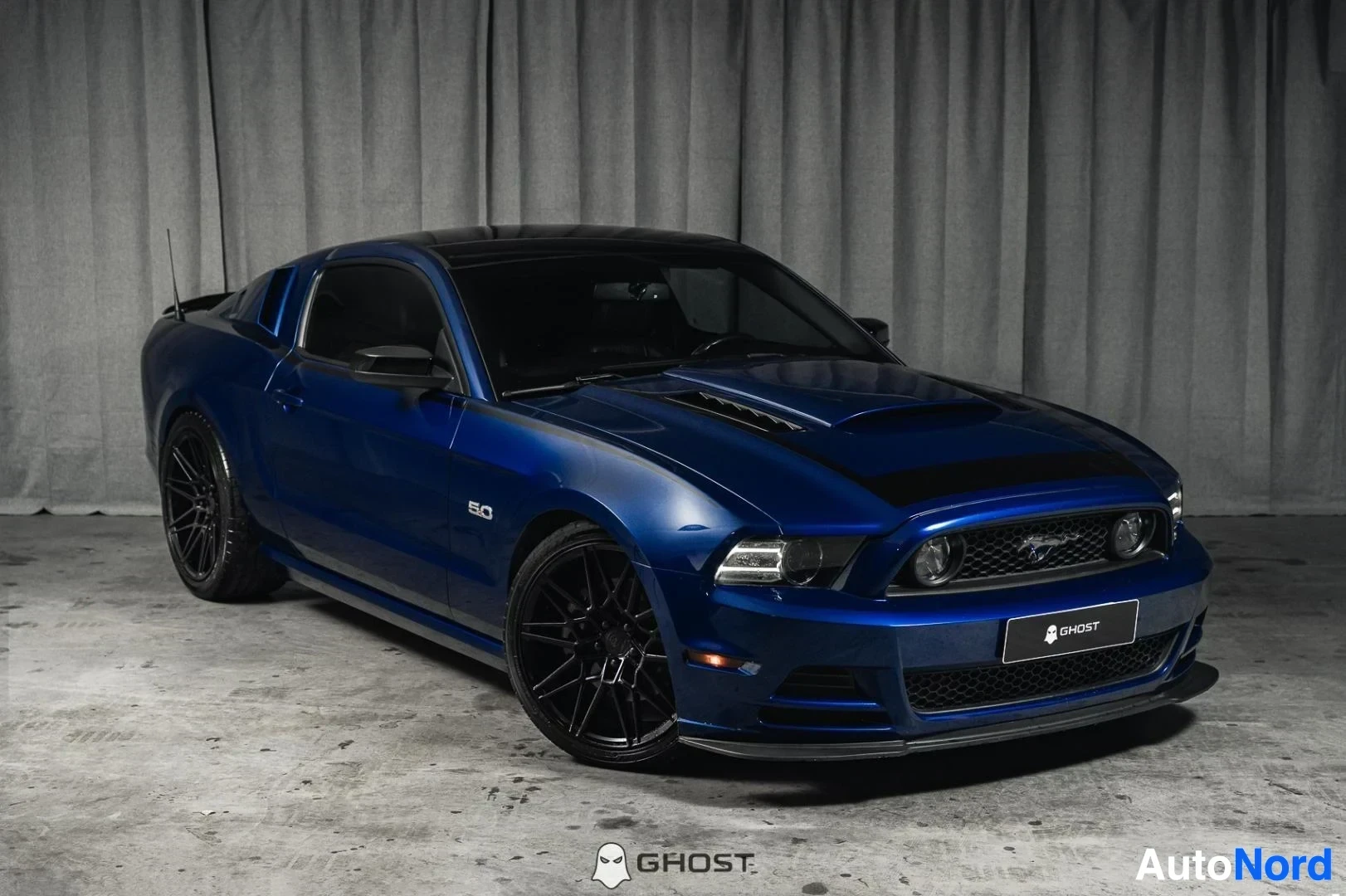 Etuviisto, nokka oikealle: Sininen Ford Mustang GT 5.0 coupe kuvattuna kolmeneljänneksestä edestä vasemmalta studiotaustaa vasten.