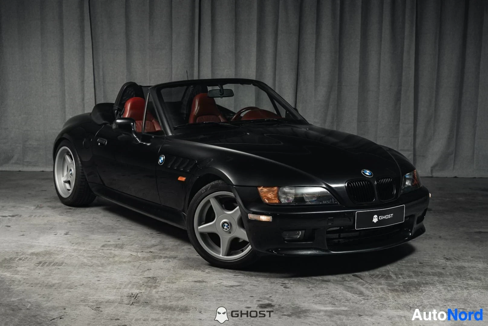 Etuviisto, nokka oikealle: Musta BMW Z3 Roadster, koko ajoneuvo näkyvissä, katto auki, punainen nahkasisusta, studiotausta
