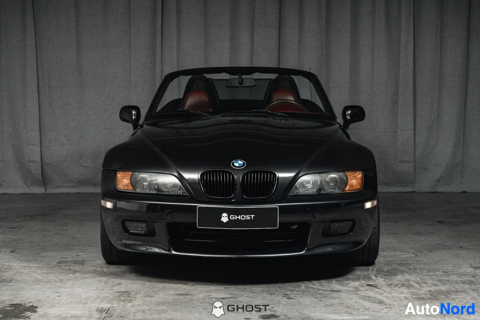 Edestä: Musta BMW Z3 Roadster, koko ajoneuvo näkyvissä, keula ja ajovalot, katto auki, studiotausta