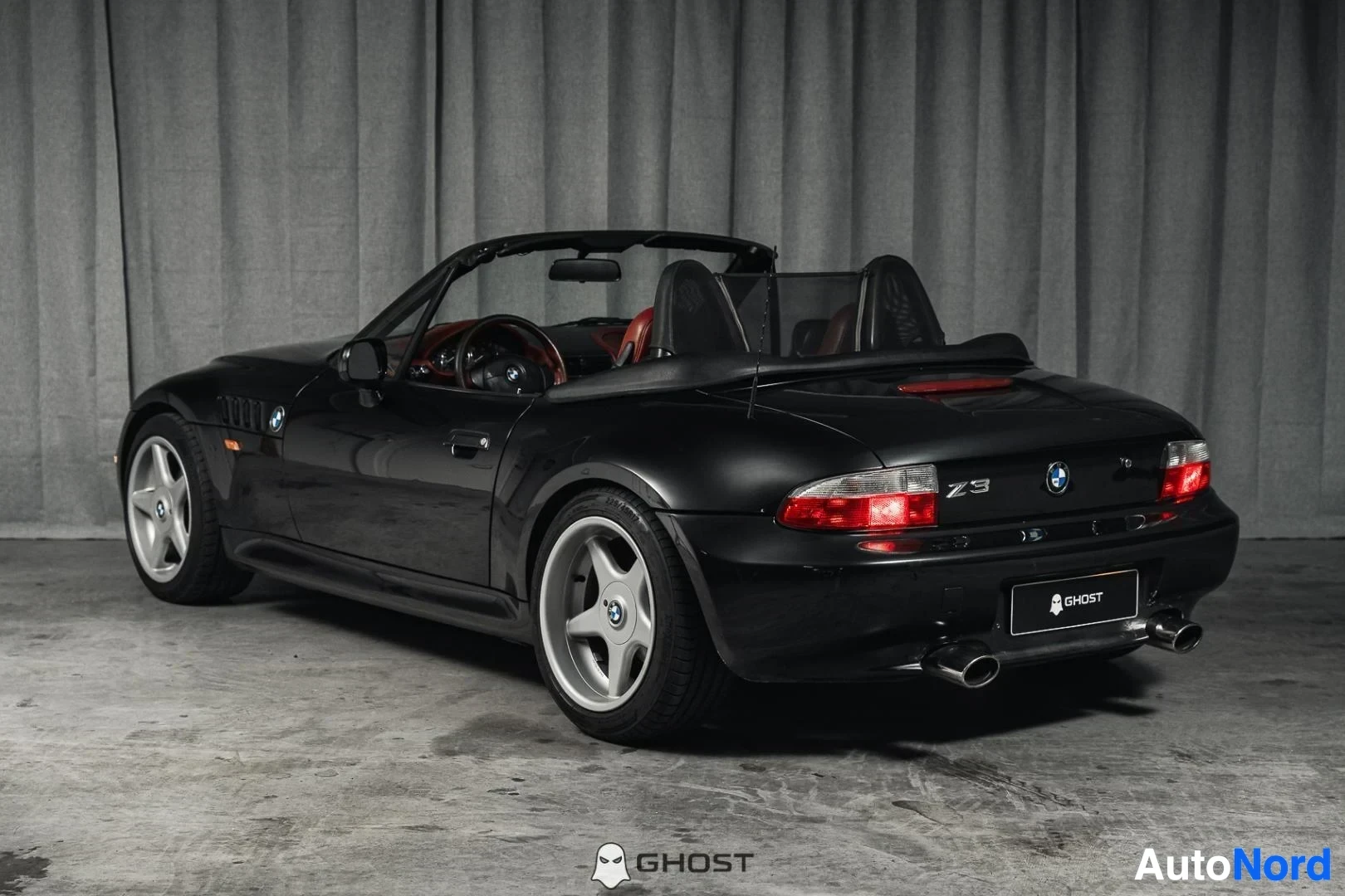 Takaviisto: Musta BMW Z3 Roadster, koko ajoneuvo näkyvissä, takavalot ja kylki, katto auki, studiotausta