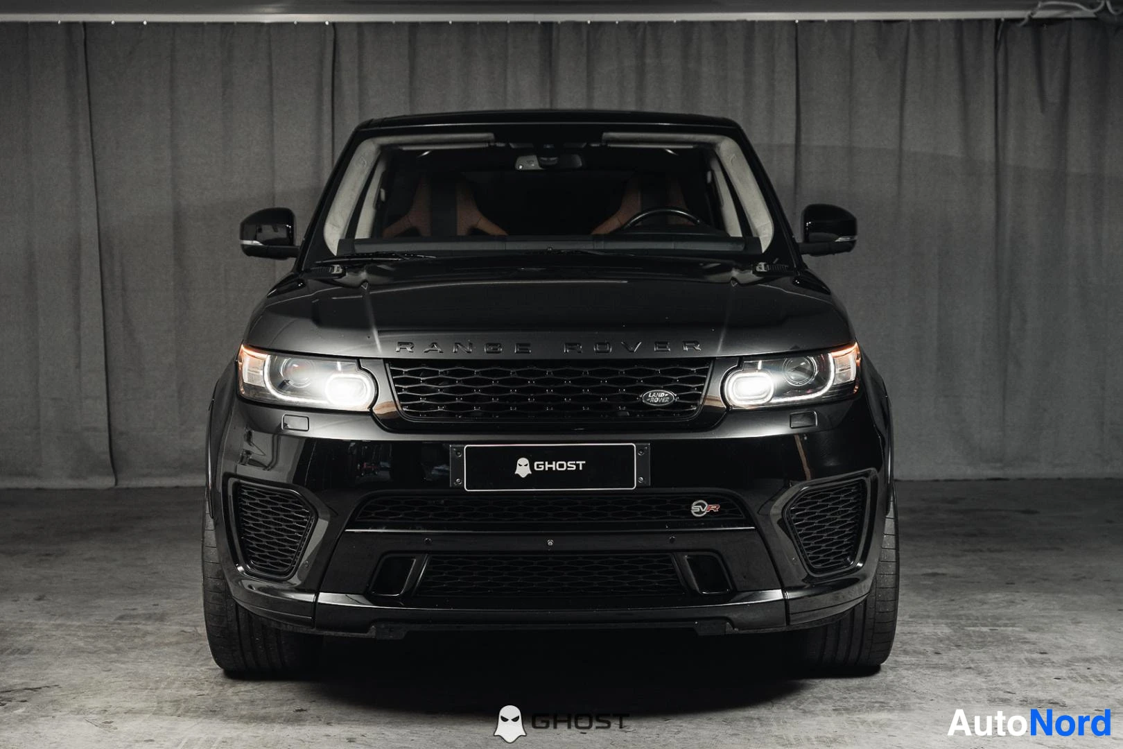 Edestä: Musta Land Rover Range Rover Sport, koko ajoneuvo näkyvissä, ajovalot päällä, studiotausta