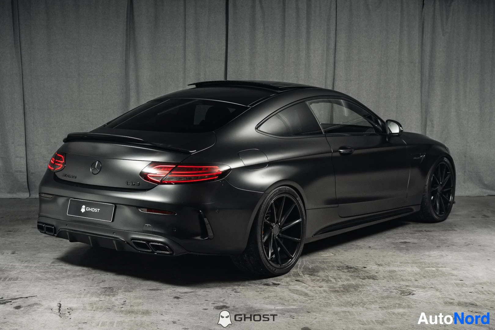 Takaviisto: Mattamusta Mercedes-Benz C 63 AMG coupé, koko ajoneuvo näkyvissä, takavalot päällä, studiotausta