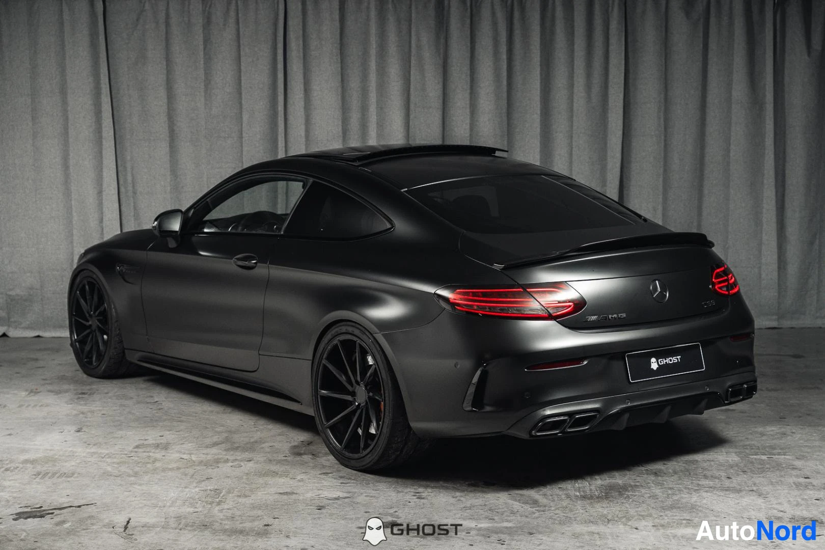 Takaviisto: Mattamusta Mercedes-Benz C 63 AMG coupé, koko ajoneuvo näkyvissä sivusta ja takaa, studiotausta