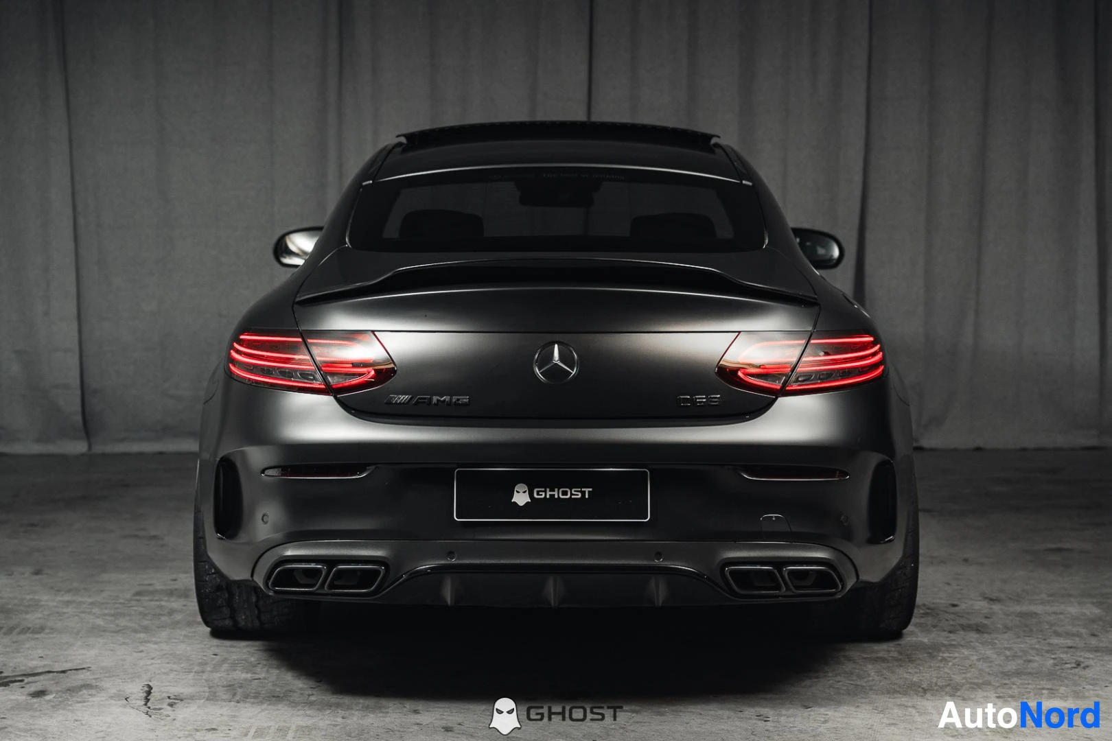 Takaa: Mattamusta Mercedes-Benz C 63 AMG coupé, koko ajoneuvo näkyvissä, takavalot ja kaksoispakoputket, studiotausta