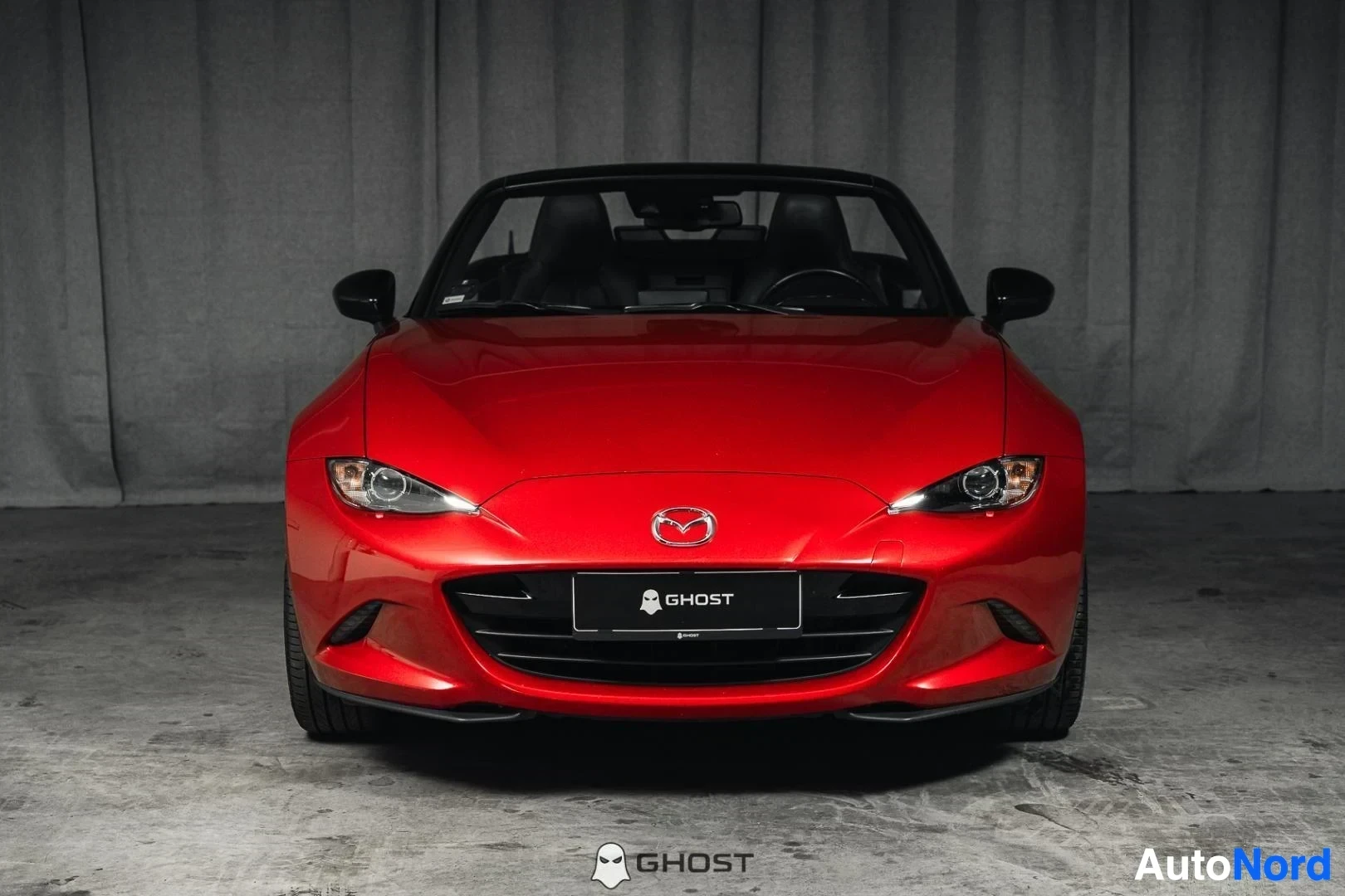 Edestä: Punainen Mazda MX-5, koko ajoneuvo näkyvissä, katto avattuna, studiotausta