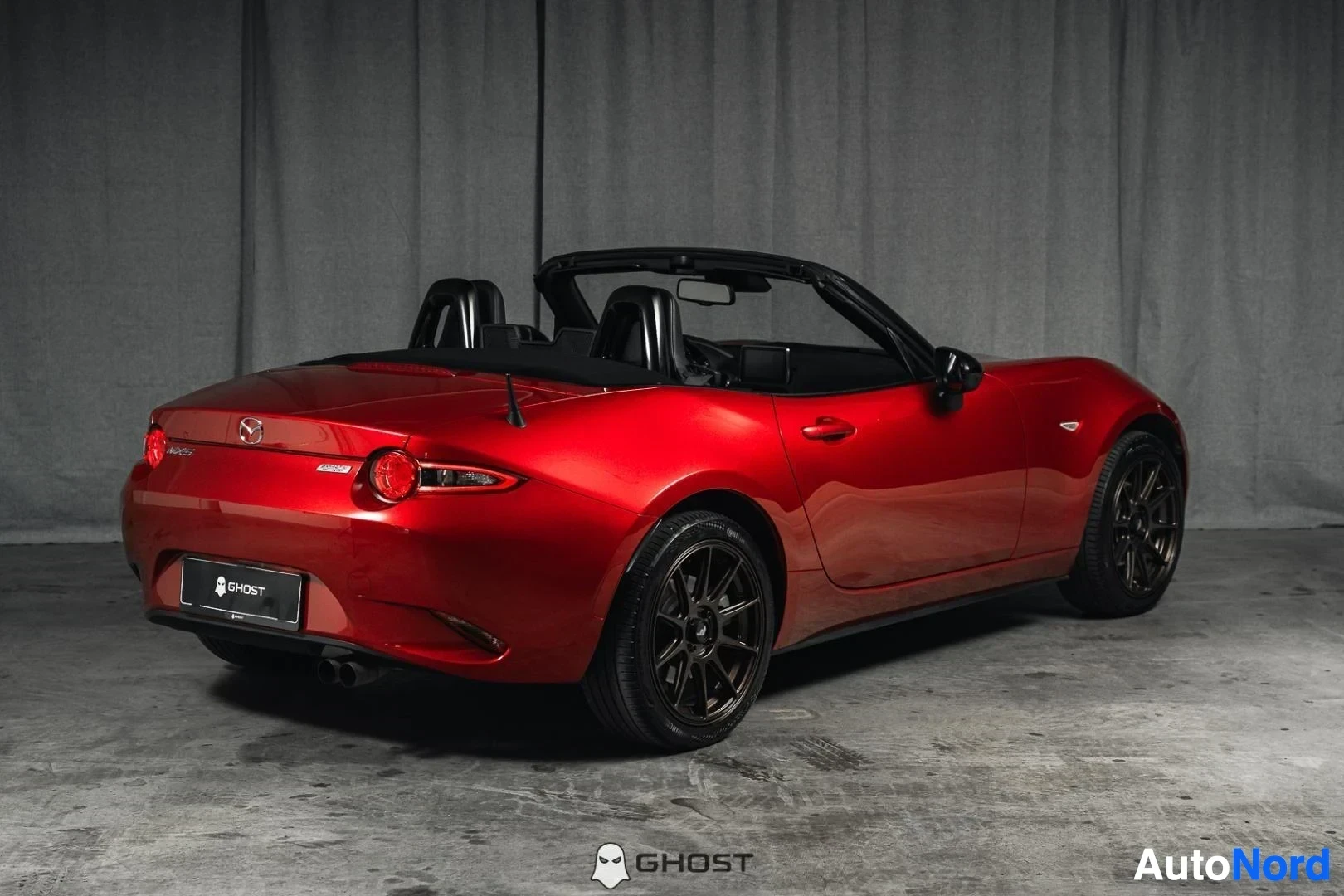 Takaviisto: Punainen Mazda MX-5, koko ajoneuvo näkyvissä, katto avattuna, studiotausta