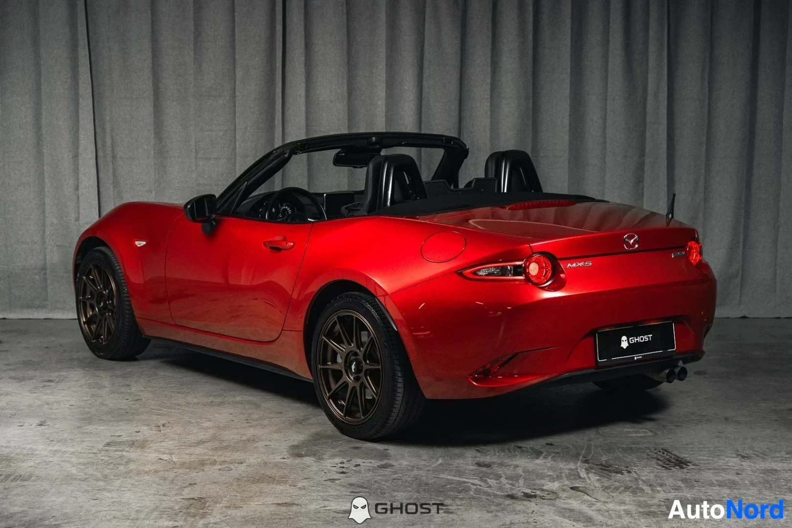 Takaviisto: Punainen Mazda MX-5, koko ajoneuvo näkyvissä sivusta ja takaa, katto avattuna, studiotausta