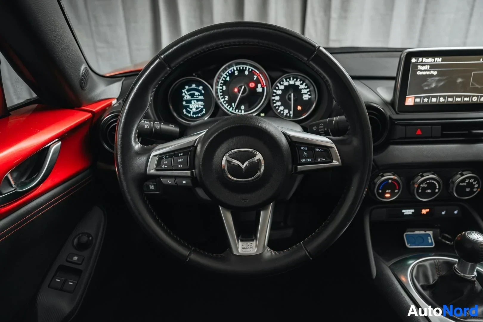 Ohjaamo: Punainen Mazda MX-5, ohjauspyörä ja mittaristo, keskinäyttö taustalla