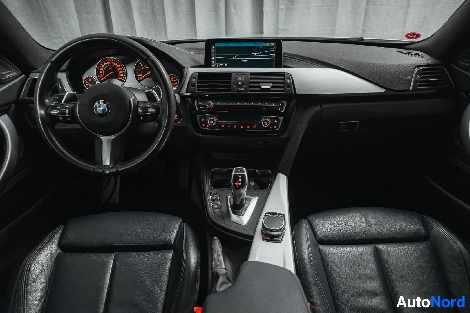 Ohjaamo: Hopeanharmaa BMW 440i F36 Gran Coupé, kojelauta, keskinäyttö ja etuistuimet takaa kuvattuna, musta nahkaverhoilu