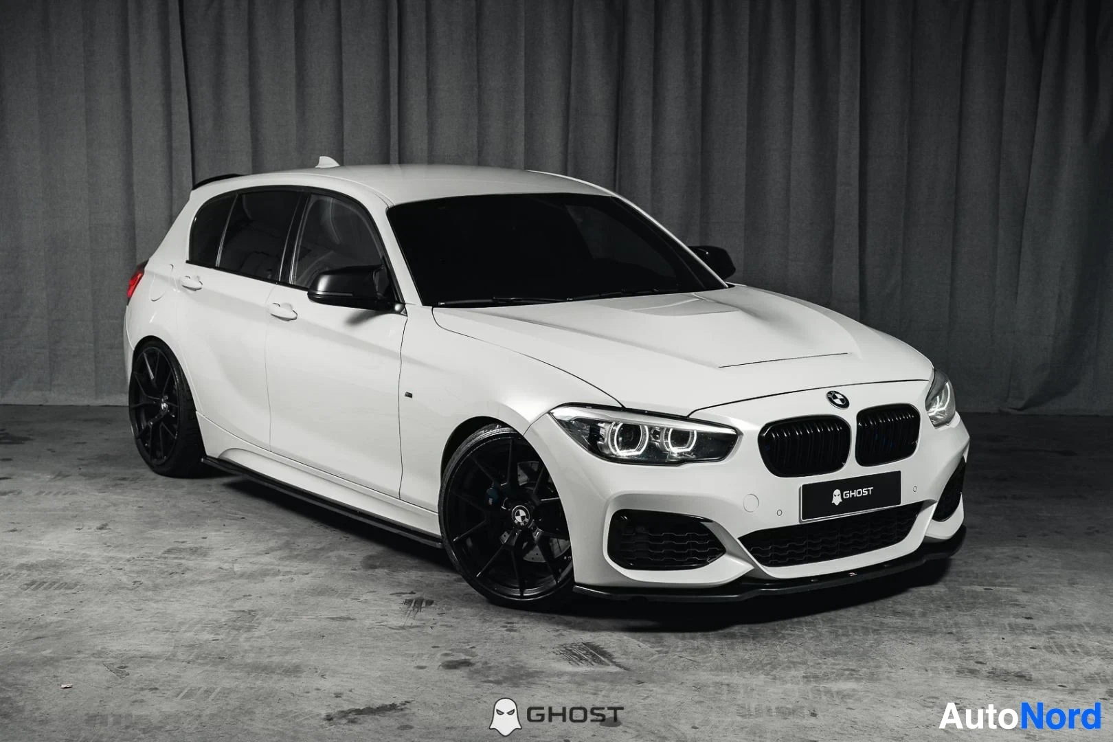 Etuviisto, nokka oikealle: Valkoinen BMW M140i F20 xDrive, koko ajoneuvo näkyvissä, M-Sport-paketti, mustat vanteet, studiotausta