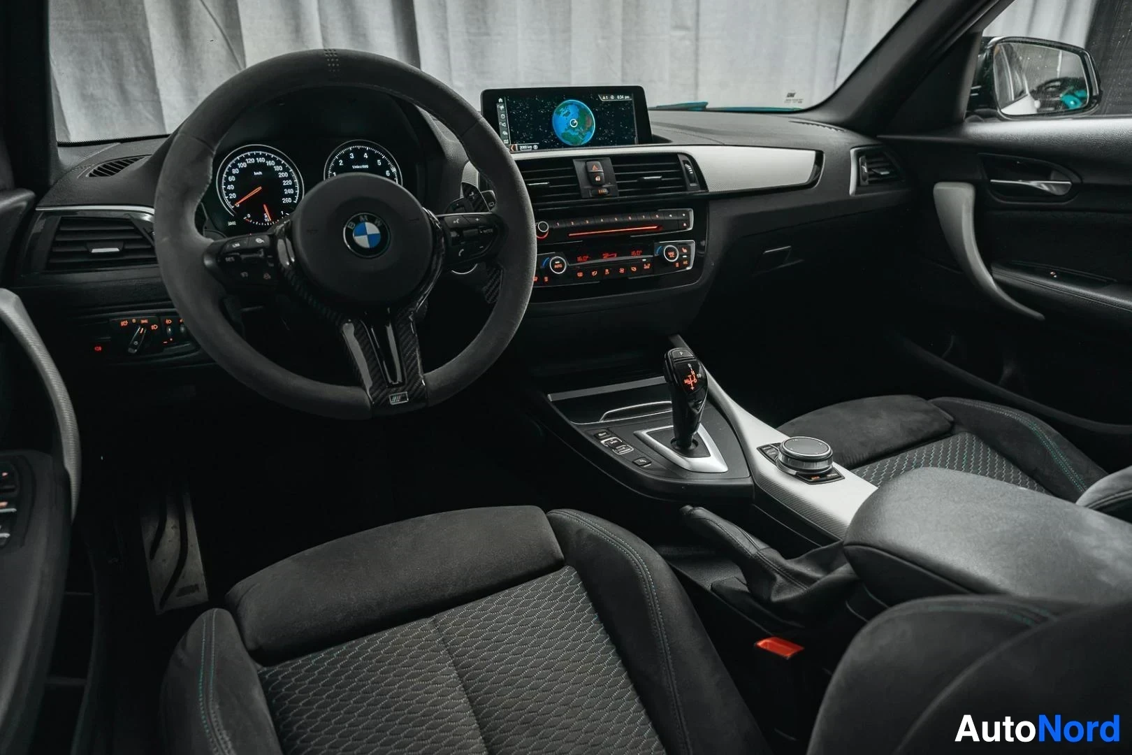 Ohjaamo: Valkoinen BMW M140i F20 xDrive, kojelauta ja etuistuimet kuljettajan ovelta kuvattuna, tumma verhoilu