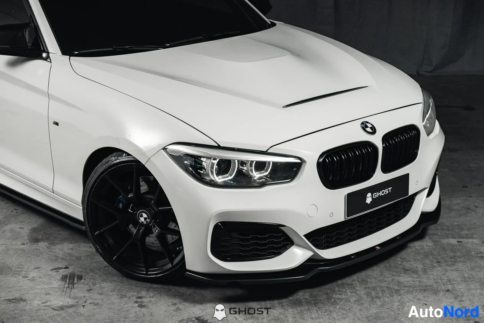 Etuviisto, nokka oikealle: Valkoinen BMW M140i F20 xDrive, lähikuva keulasta ja mustasta etuvanteesta