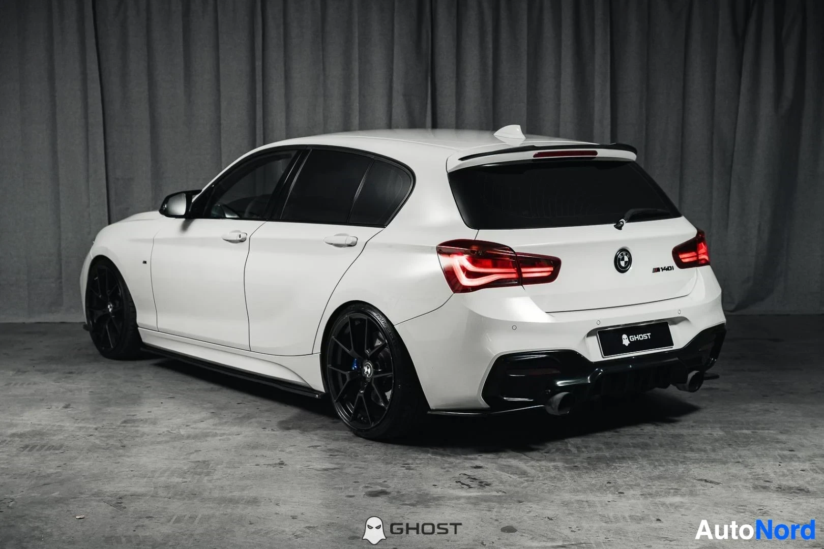 Takaviisto: Valkoinen BMW M140i F20 xDrive, koko ajoneuvo näkyvissä, takavalot ja kylki, mustat vanteet, studiotausta