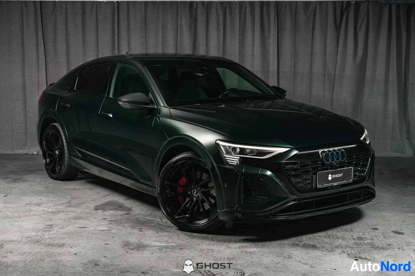 Etuviisto, nokka oikealle: Tummanvihreä Audi Q8 e-tron Sportback, koko ajoneuvo näkyvissä, mustat vanteet, studiotausta