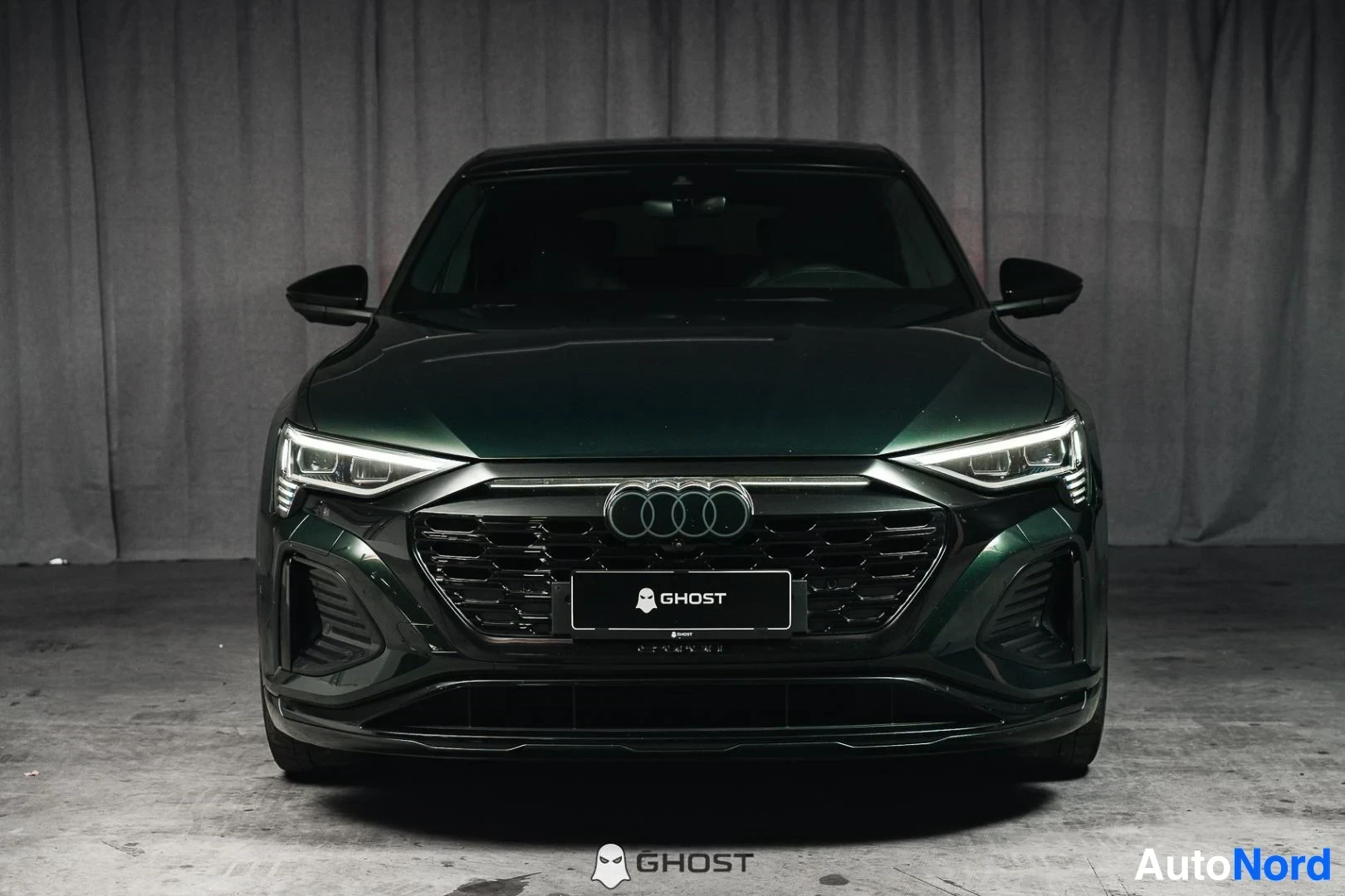 Edestä: Tummanvihreä Audi Q8 e-tron Sportback, koko ajoneuvo näkyvissä, suljettu säleikkö ja LED-ajovalot