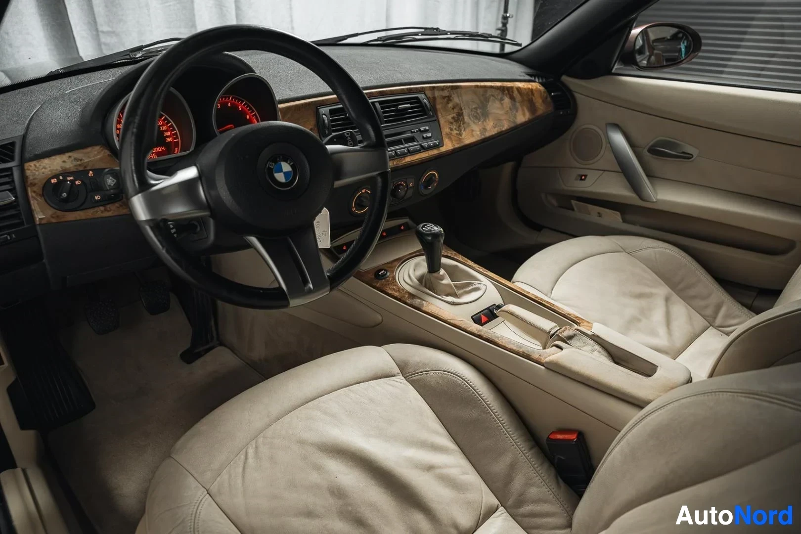 Ohjaamo: Tummanpunainen BMW Z4 E85 Roadster, kojelauta ja ohjauspyörä kuljettajan ovelta kuvattuna, beige nahkaverhoilu, puukoristelu