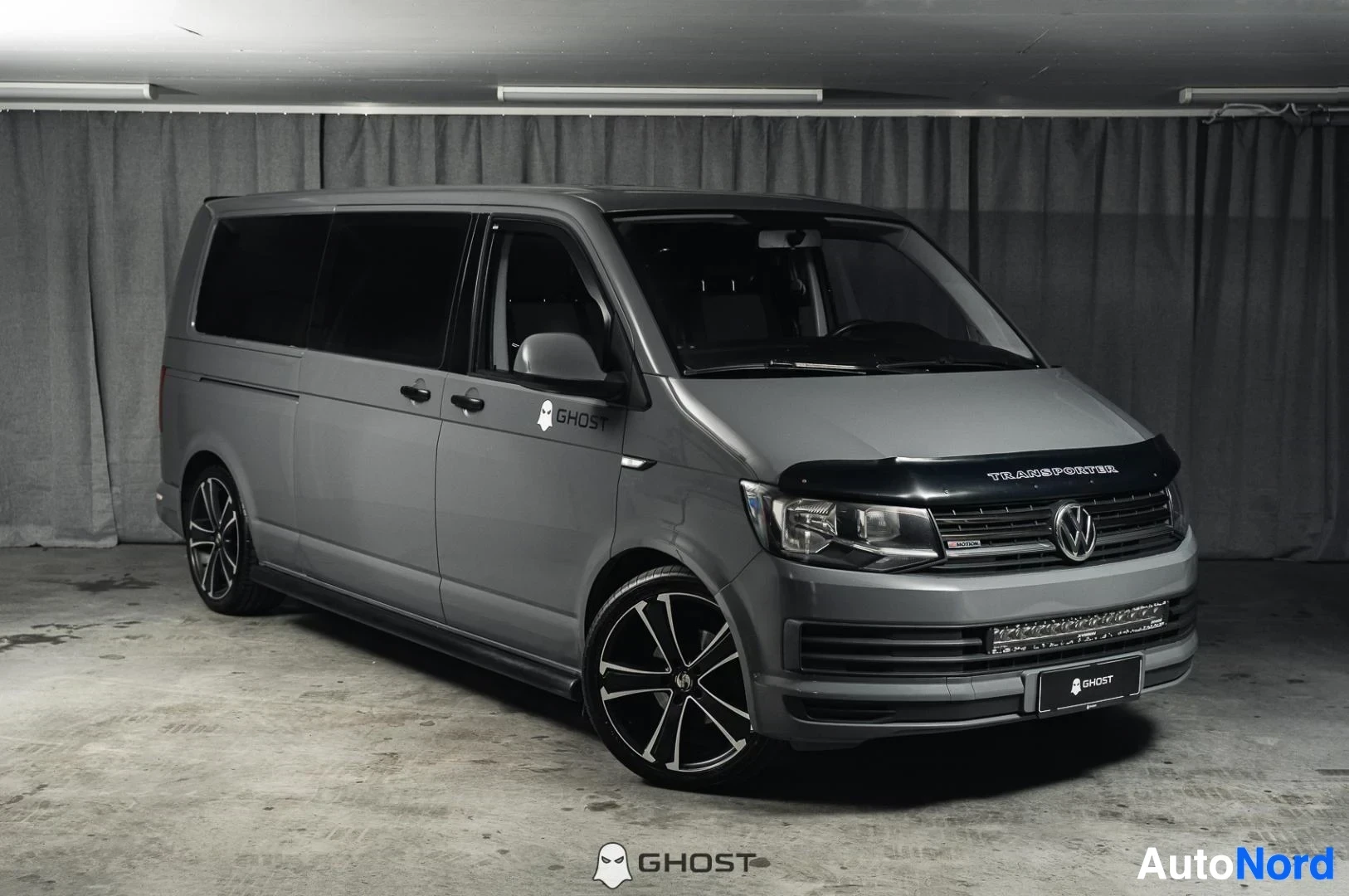 Etuviisto, nokka oikealle: Harmaa Volkswagen Transporter, koko ajoneuvo näkyvissä, pitkä pakettiauto, tummat vanteet, studiotausta
