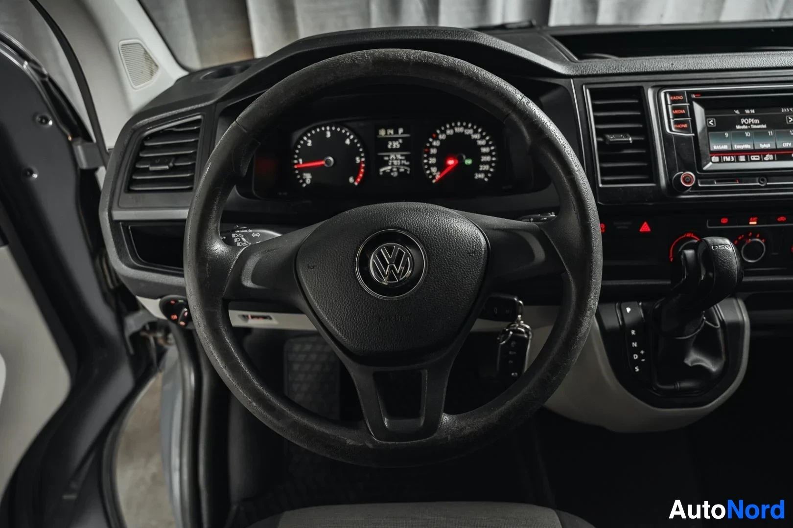 Ohjaamo: Harmaa Volkswagen Transporter, ohjauspyörä, mittaristo ja keskinäyttö kuljettajan puolelta