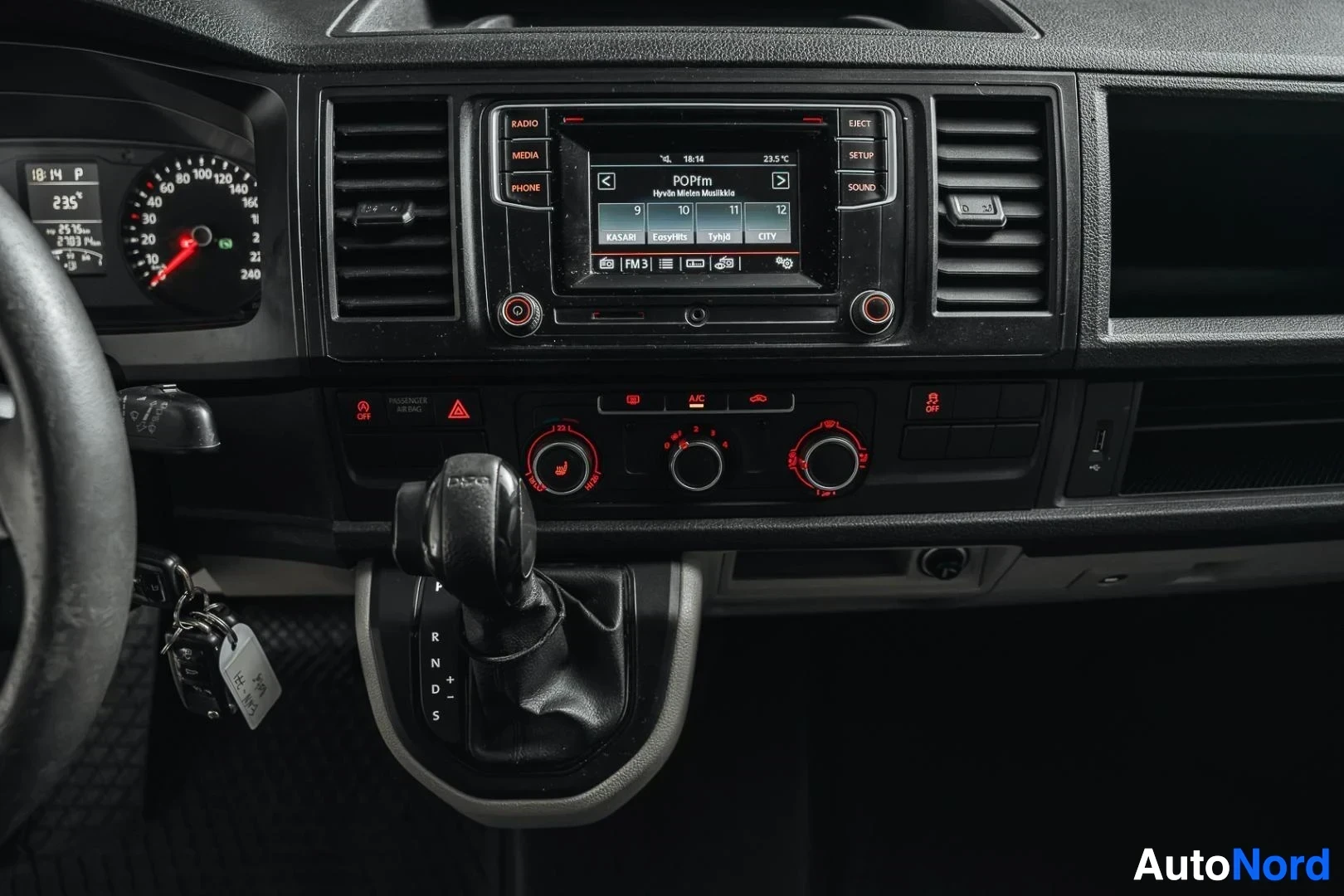 Yksityiskohta: Harmaa Volkswagen Transporter, keskikonsoli, radio, ilmastoinnin säätimet ja vaihdekeppi